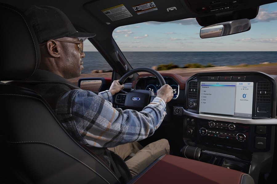 A person behind a wheel driving a 2022 Ford F-150® with the ocean in the background