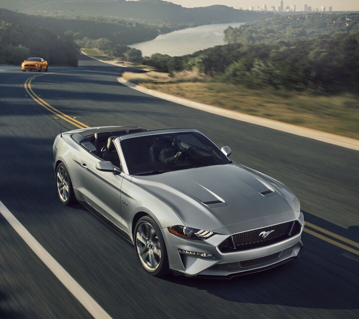 Un Ford Mustang  2021 convertible con el techo abierto andando en una autopista de dos carriles 