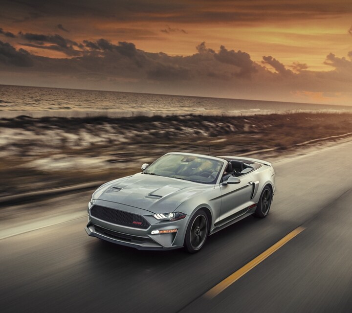 A 2023 Ford Mustang® convertible model being driven on an oceanside highway