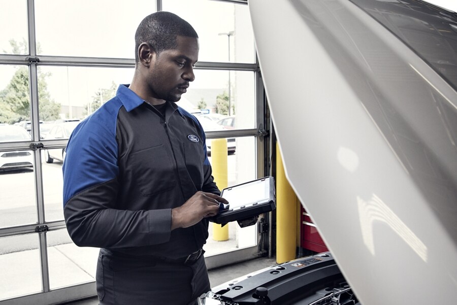 Técnico de un Concesionario Ford usando una computadora de diagnóstico en un motor