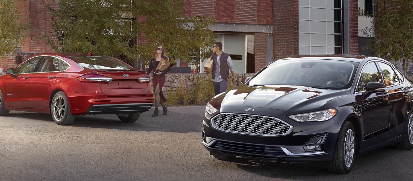 Two Ford vehicles parked outside of a building with people walking by