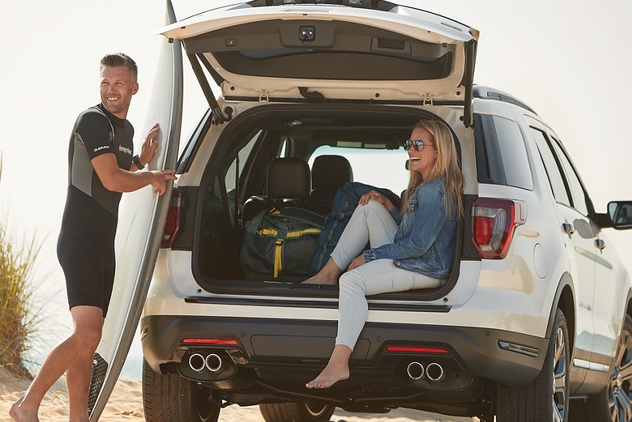 Una pareja con una tabla de surf en la parte trasera de una SUV Ford estacionada.