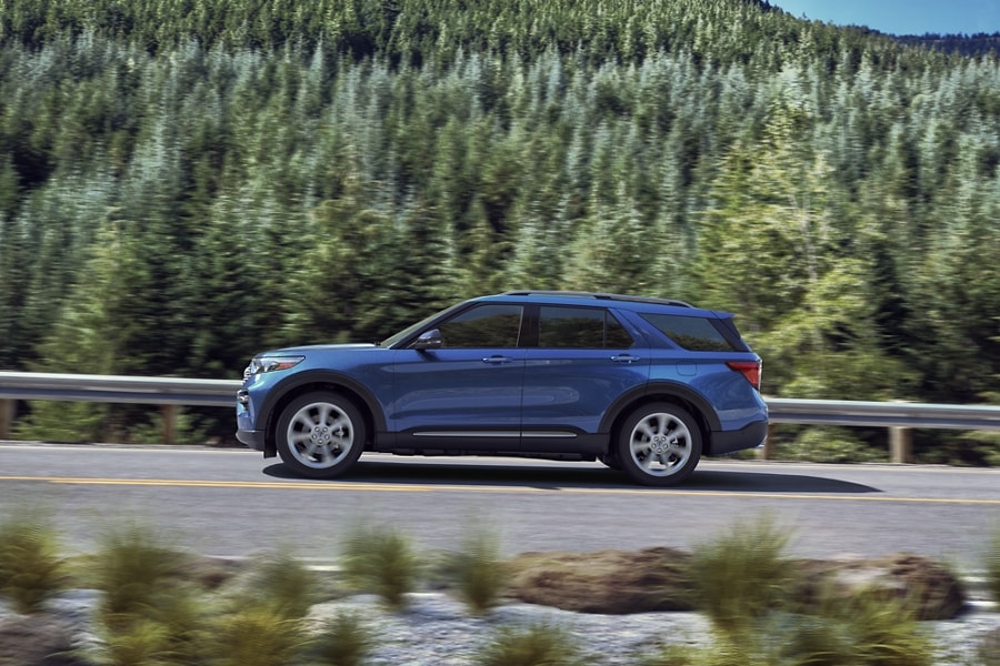 Side view of a Ford Explorer Limited Hybrid Platinum in Atlas Blue driving along a tree lined highway