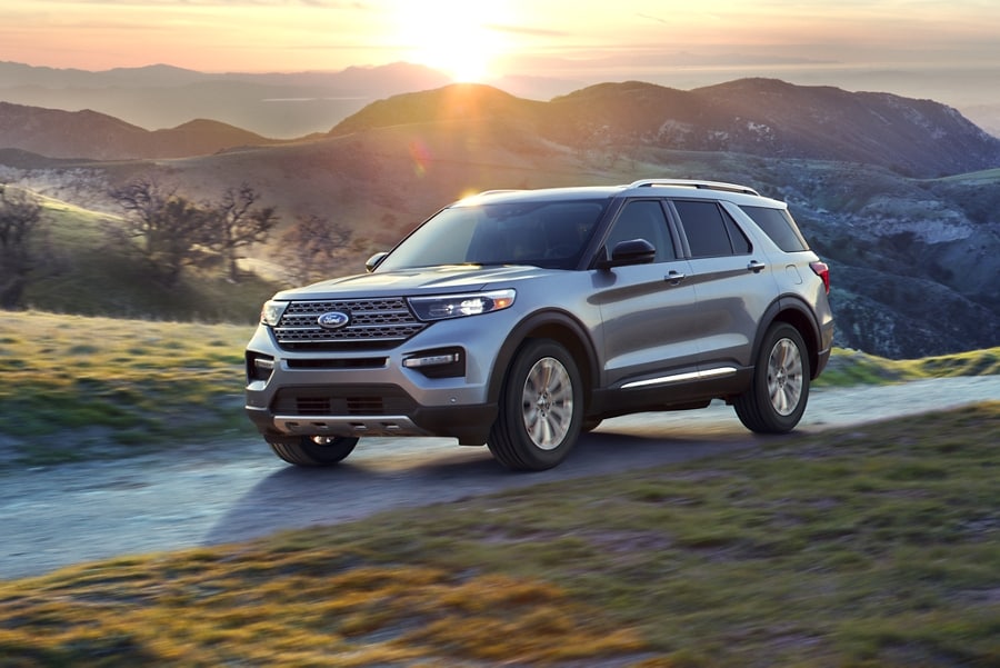 Front three quarter view of a Ford Explorer Limited Hybrid being driven on a rural mountain road at sunset