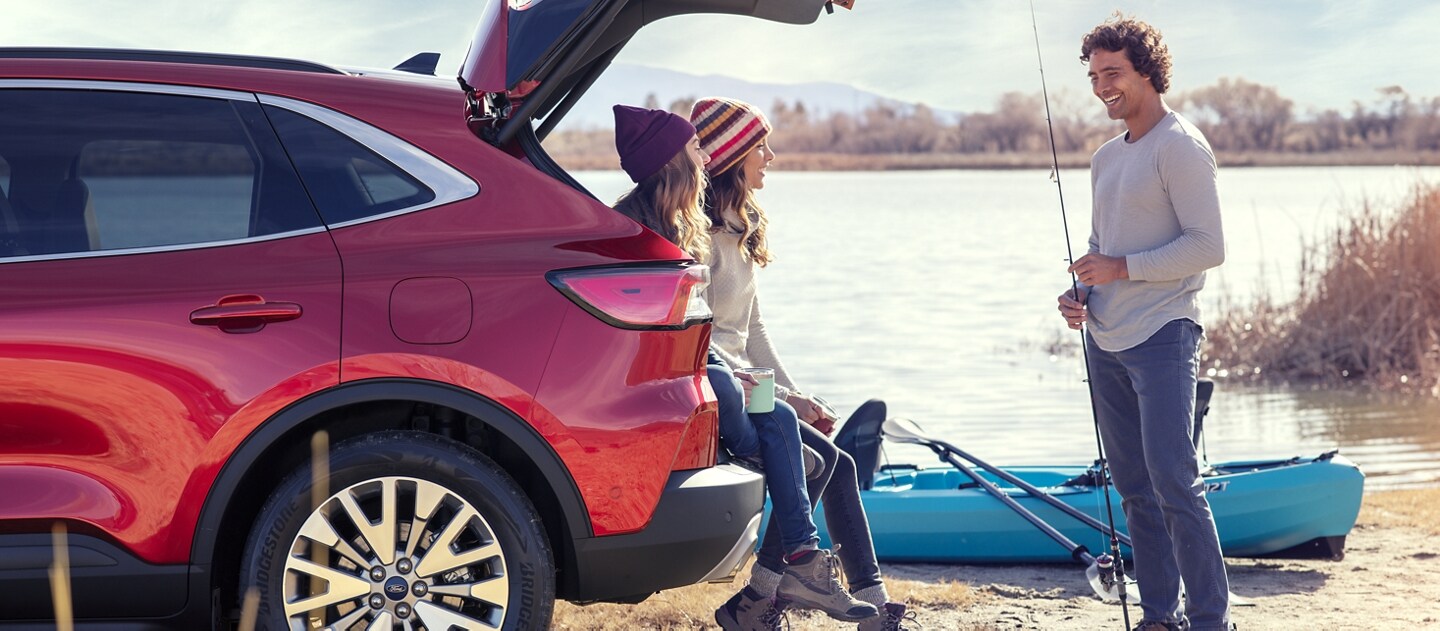 Side view of an Escape parked on the beach with the liftgate open and people sitting in the back