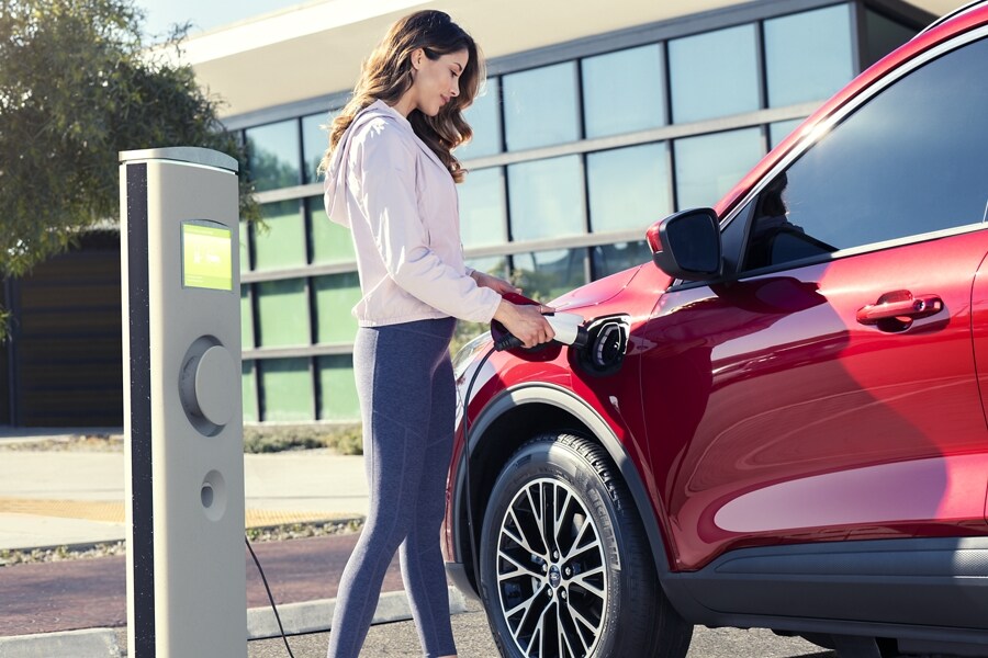 A woman is shown plugging in a Ford Escape Plug In Hybrid at a charging station