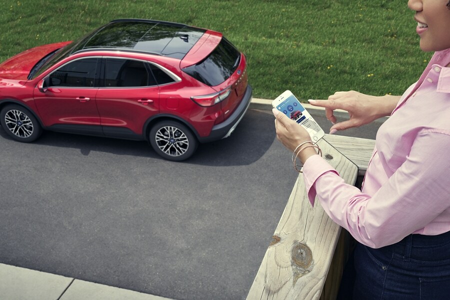 Vista desde arriba de una mujer tocando un dispositivo móvil cerca de una Ford Escape Plug In Hybrid estacionada