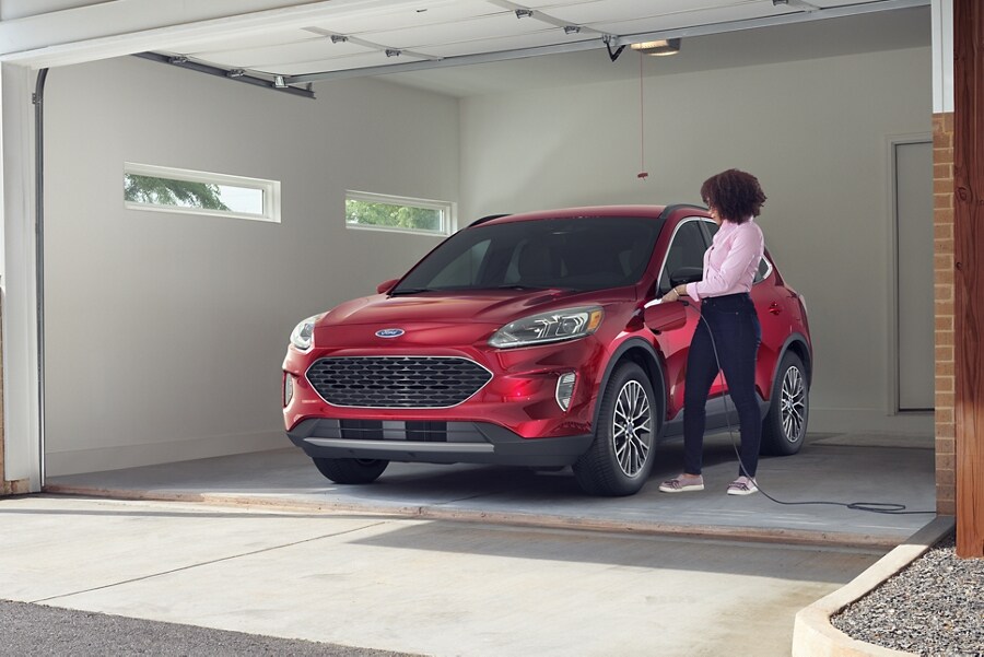 Vista frontal de una mujer parada en un garaje cerca de una Ford Escape Plug In Hybrid estacionada