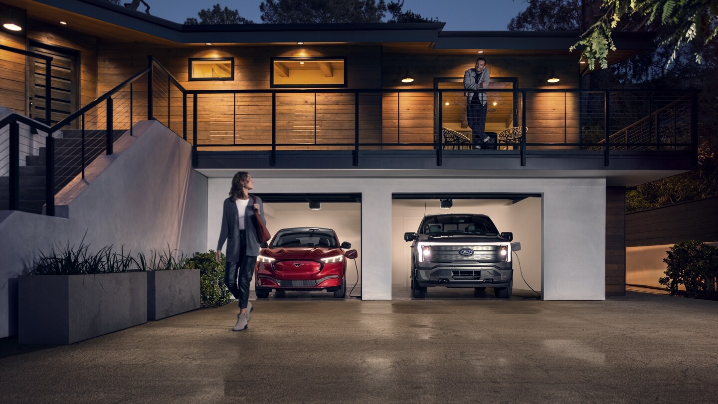 A 2022 Ford Mustang Mach-E® and a Ford F-150® Lightning™ are being charged in a garage at night near two people