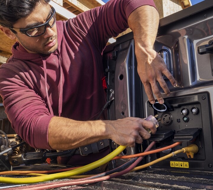 A closeup of a man plugging equipment into the Pro Power Onboard feature of a 2023 Ford F-150® Lightning®