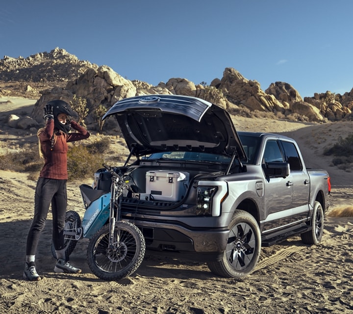 Two people packing the FRUNK (front trunk) of a 2023 Ford F-150® Lightning®. The vehicle is parked at a campsite