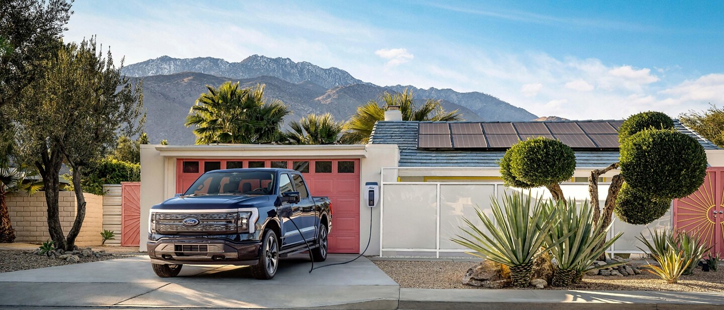 A black 2023 Ford F-150® Lightning® backed into the driveway of a suburban home. The landscape feels arid, almost desert like