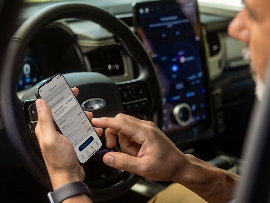 Closeup of a driver parked in a 2023 Ford F-150® Lightning®, updating his truck's software with his mobile device and Ford Power Up