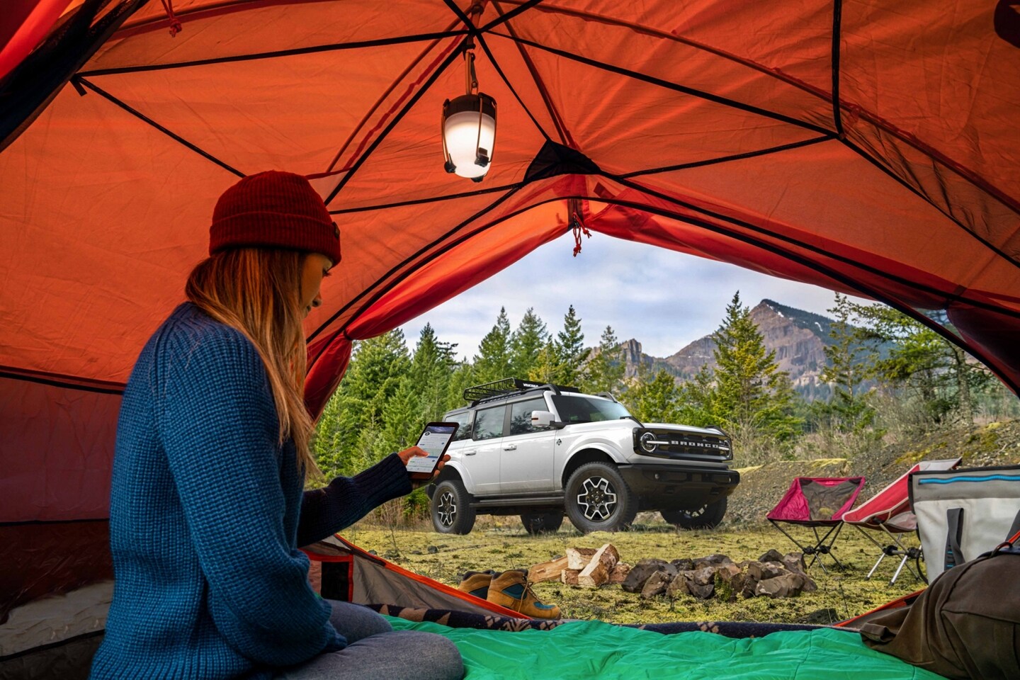 A woman in a tent looking at her smartphone with a 2023 Ford Bronco® SUV in the background
