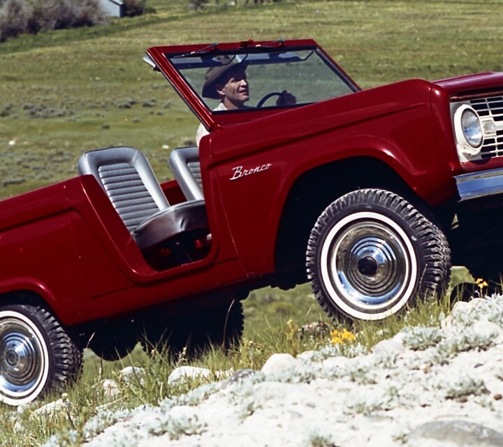 1966 Ford Bronco Roadster in Rangoon Red climbing a steep incline near a tall mountain range