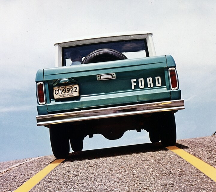 Rear view of a 1967 Ford Bronco being driven up a hill