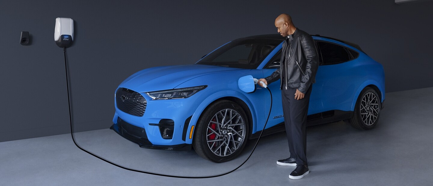 Man plugs charger into a 2022 Ford Mustang Mach-E parked in a garage