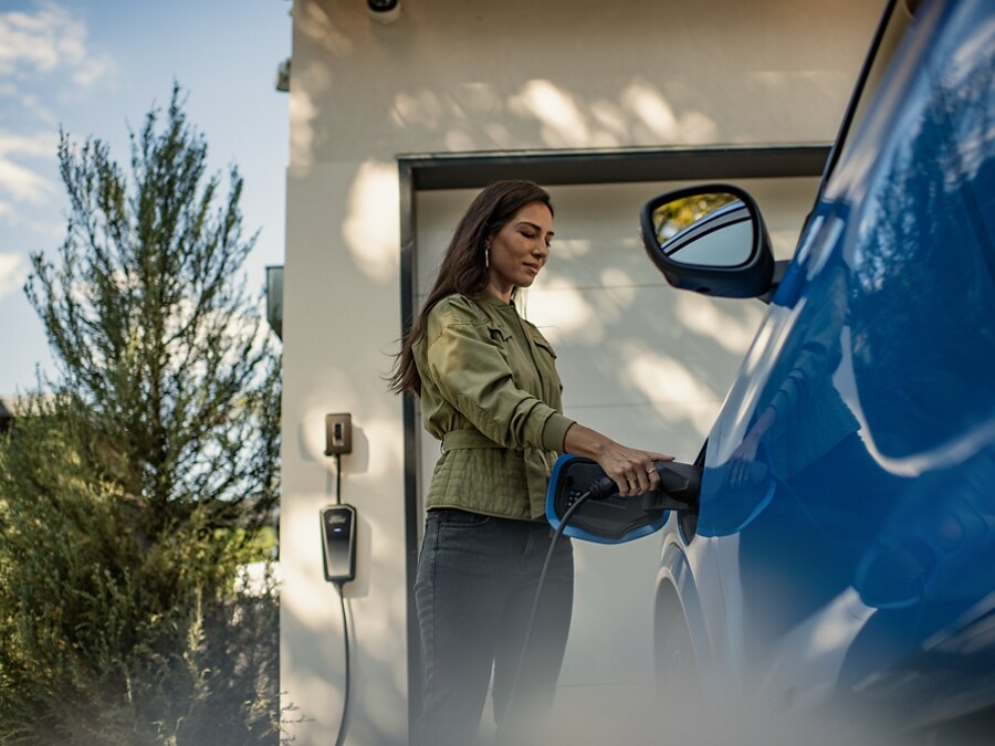 Woman placing charger into charging port on a Ford Mustang Mach-E standing outside of her garage