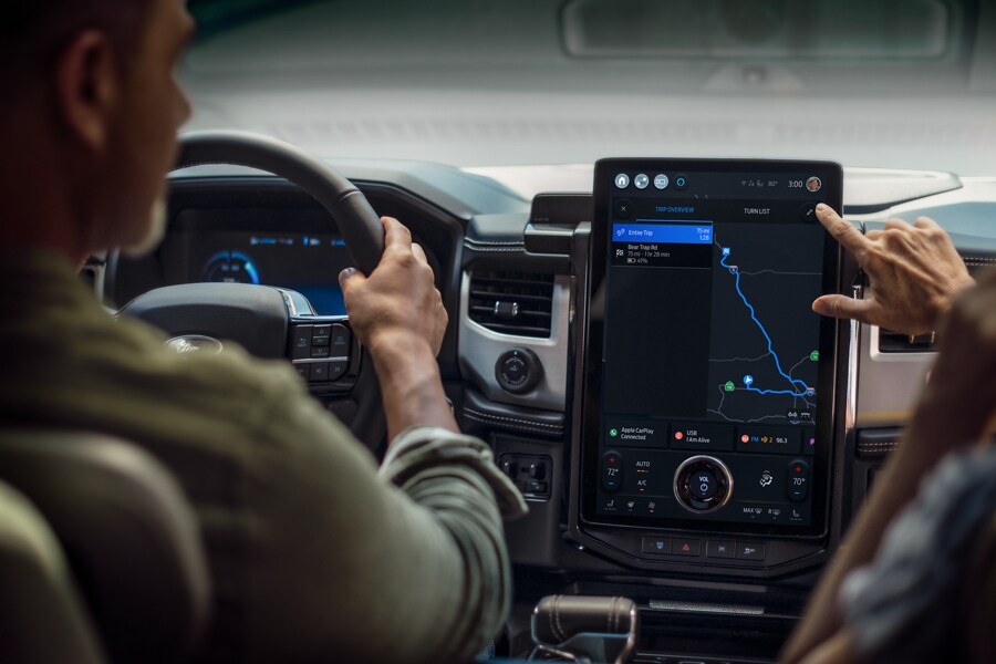 A passenger in a Ford F-150 Lightning truck touches the in-vehicle screen that shows a map.