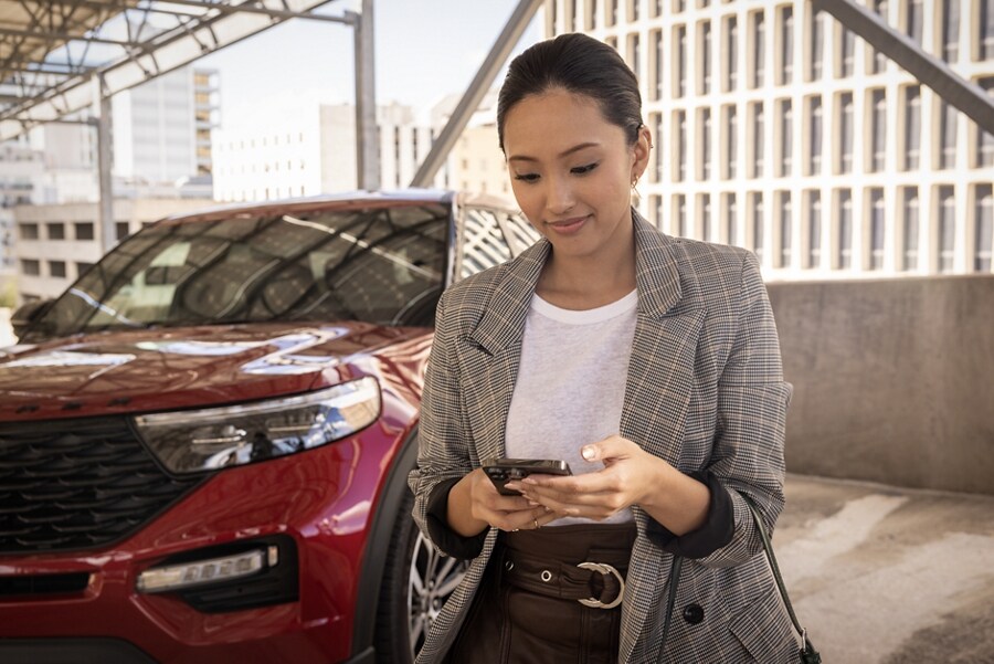 A woman looking at her iPhone walks past a Ford Explorer SUV.