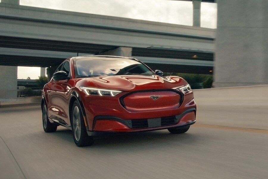 A Ford Mustang Mach-E SUV drives past an overpass on a highway.