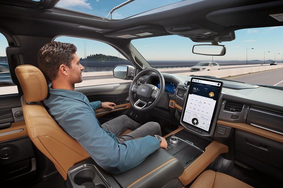 A man sits in the driver seat of a Ford Expedition SUV with his hands off the steering wheel while Ford BlueCruise is active.  