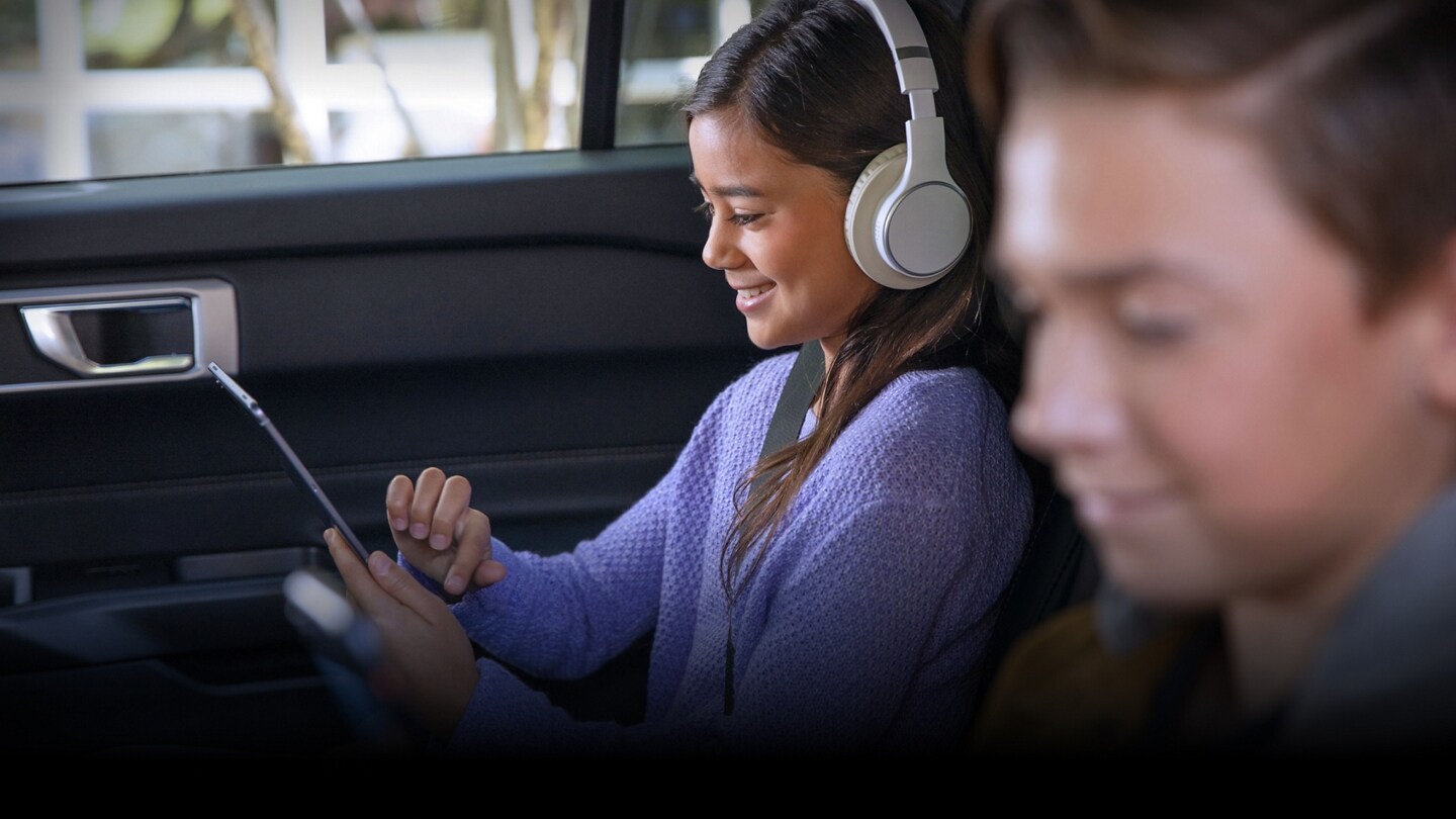 Two smiling children using mobile devices while sitting in the backseat of a Ford SUV.