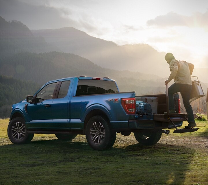 Man using the liftgate step on a 2022 Ford F-150® XLT Extended Cab in Atlas Blue at a campground