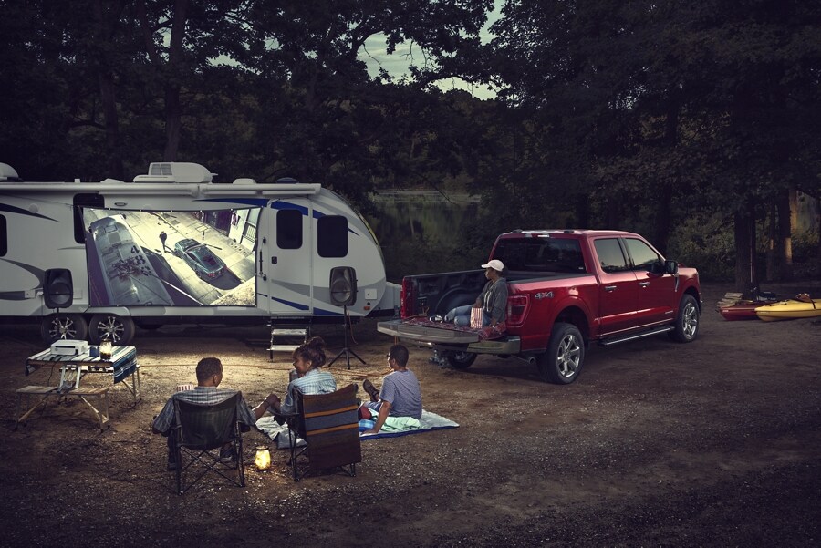 Familia en un camping viendo una película proyectada en el lateral de un vehículo recreativo con una F-150® XLT 2022 en Race Red de fondo