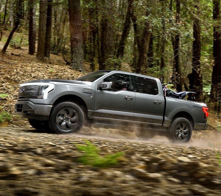 2022 Ford F-150® Lightning™ in Iconic Silver being driven on a dirt road in a wooded area