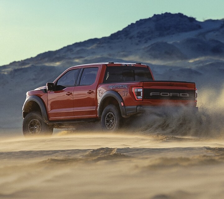 2022 Ford F-150 Raptor® in Rapid Red kicking up sand on a dune