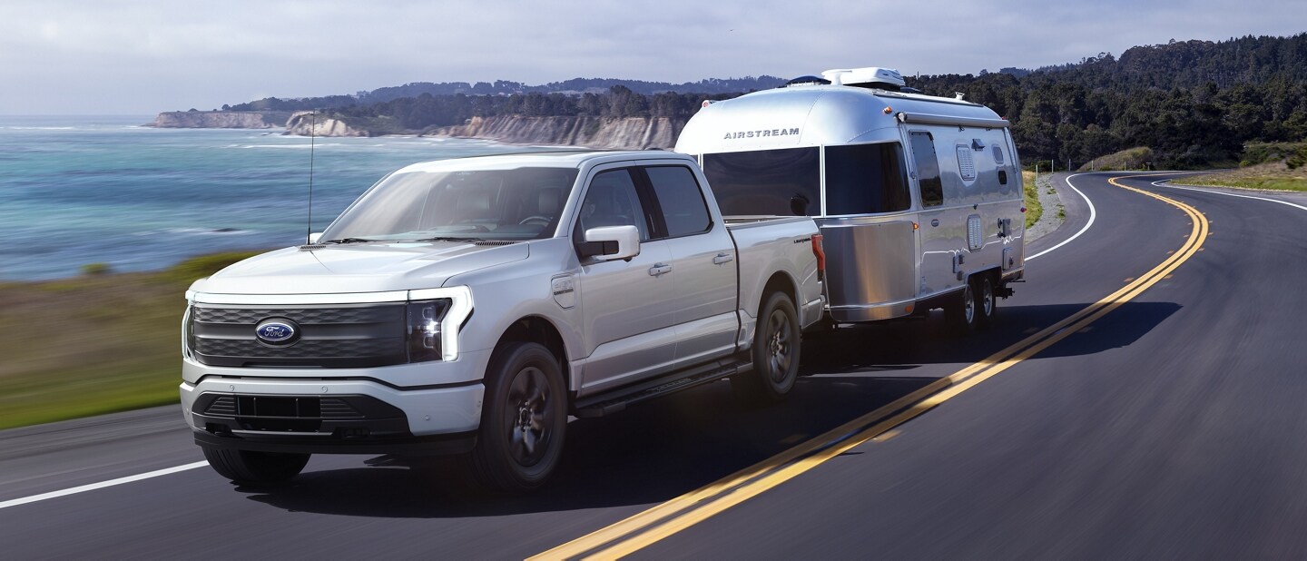 2022 Ford F-150® Lightning™ towing a camper on an oceanside road