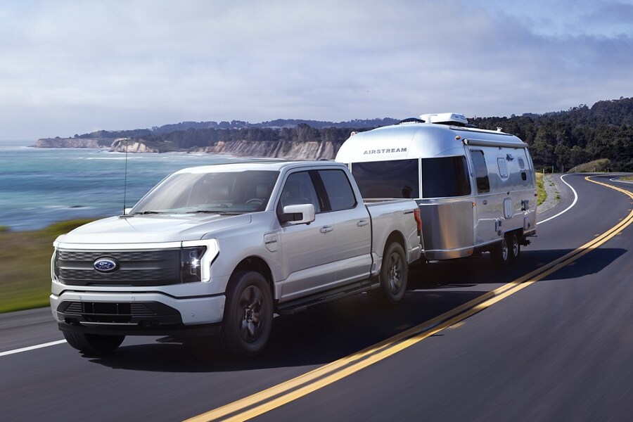 Una Ford F-150® Lightning™ 2023 remolcando una caravana en una carretera junto al mar
