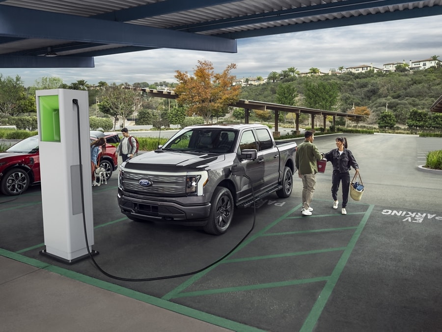 A couple unloads picnic gear as their 2023 Ford F-150 Lightning® charges at a public charging station