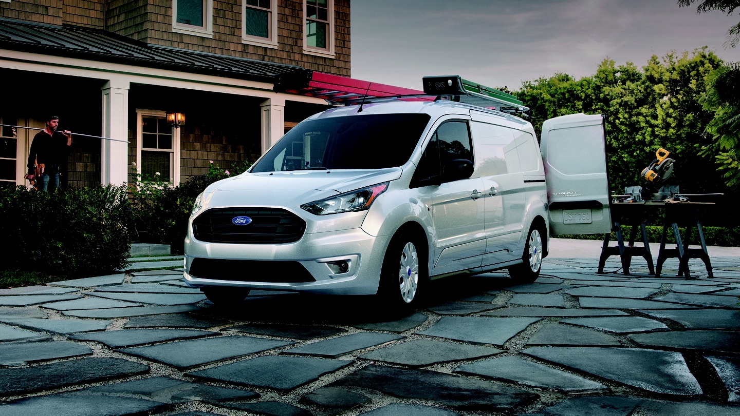 A 2023 Transit Connect Van in front of a house with home improvement builders working