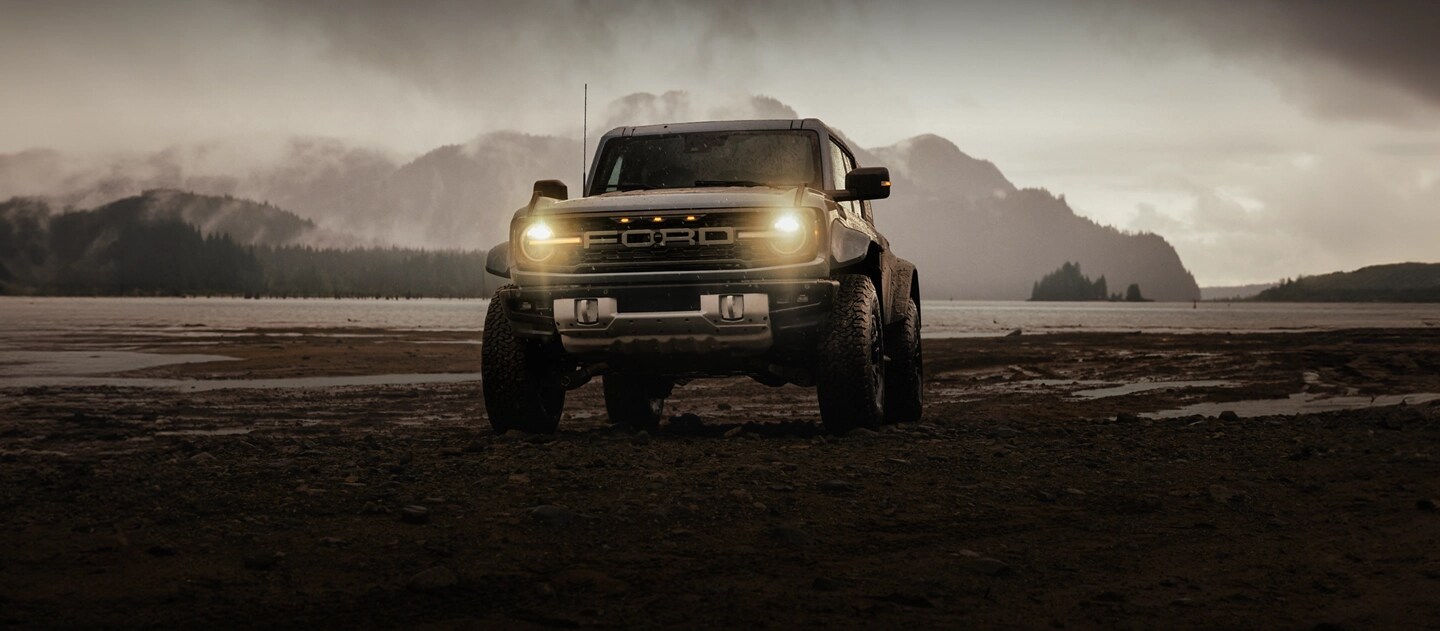 A 2025 Ford Bronco® SUV on a mud flat near a snowcapped mountain, with rain clouds threatening
