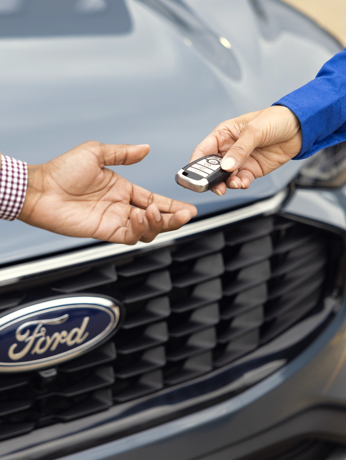 Two people, one is handing the other a key fob with a Ford vehicle in the background 