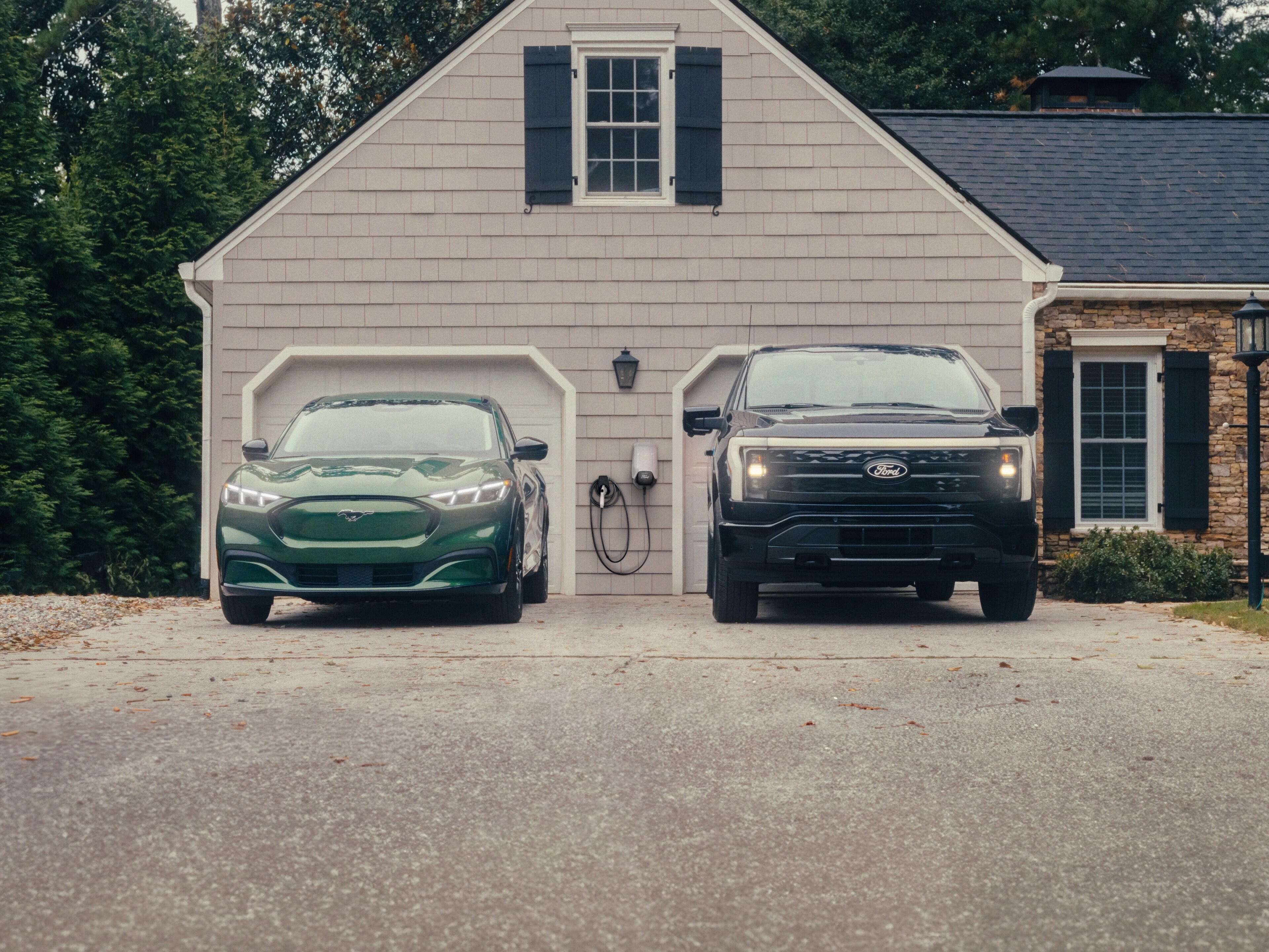Ford Mustang Mach-E® SUV and Ford F-150® Lightning® parked in the driveway in front of a double-car garage
