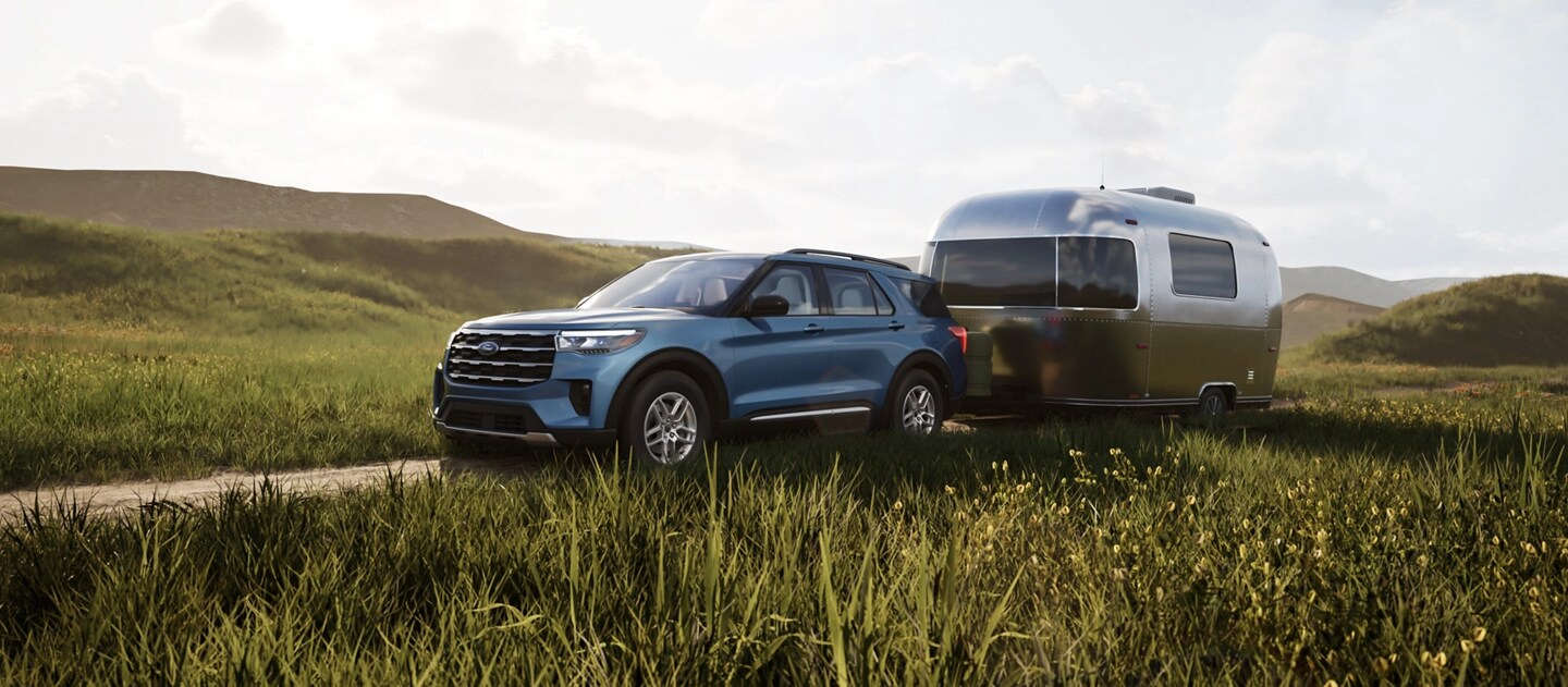 A 2025 Ford Explorer® SUV tows a camper on a path beside a field