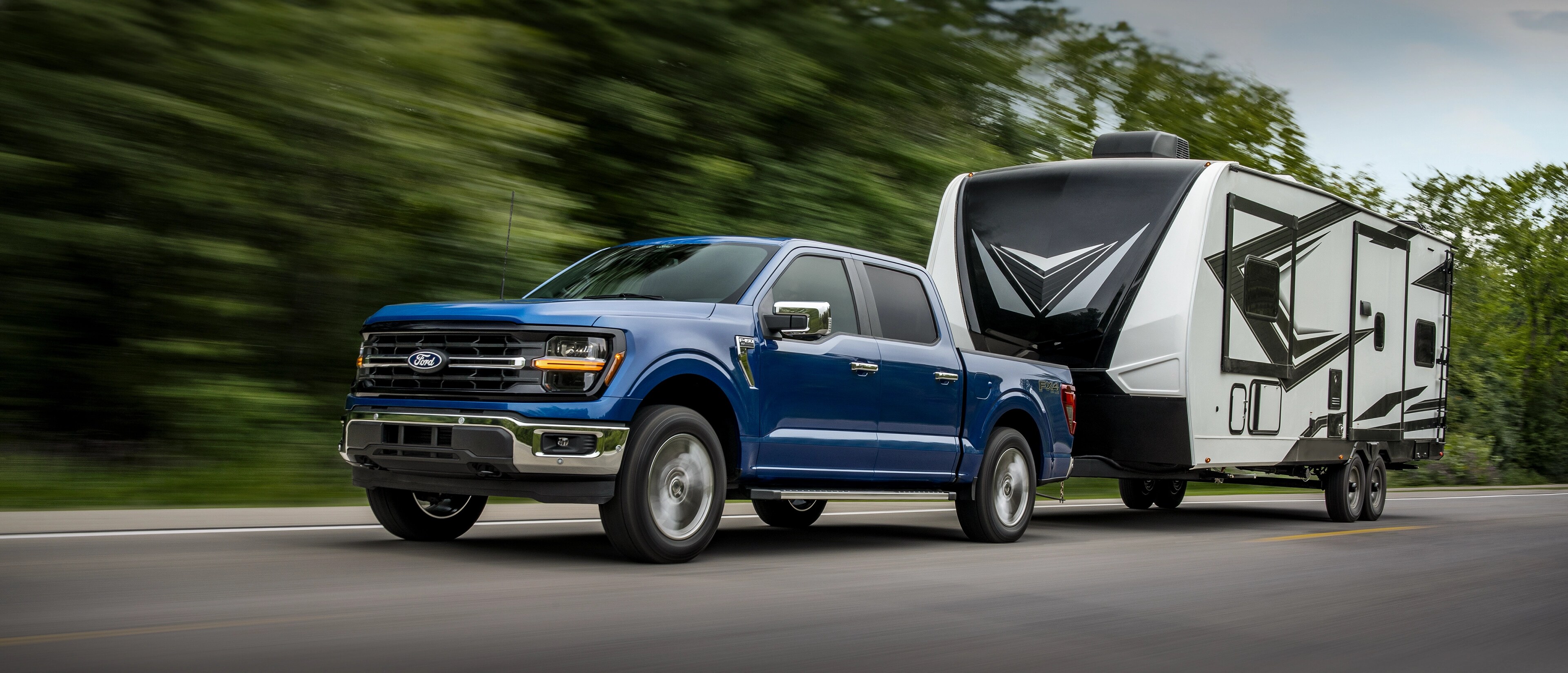 2025 Ford F-150® truck hitched to a camper trailer being driven in a wooded area