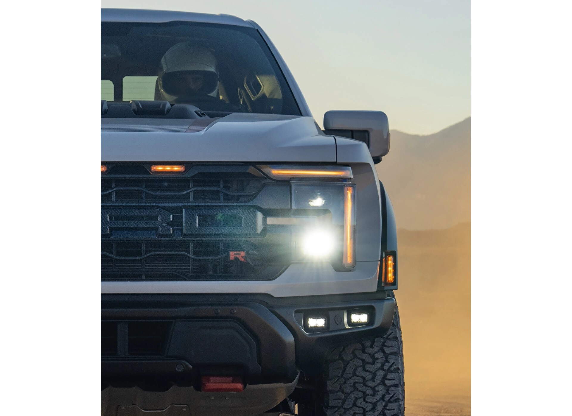 Close-up view on the grille and headlamp of a 2026 Ford F-150® Raptor® truck being driven in the desert