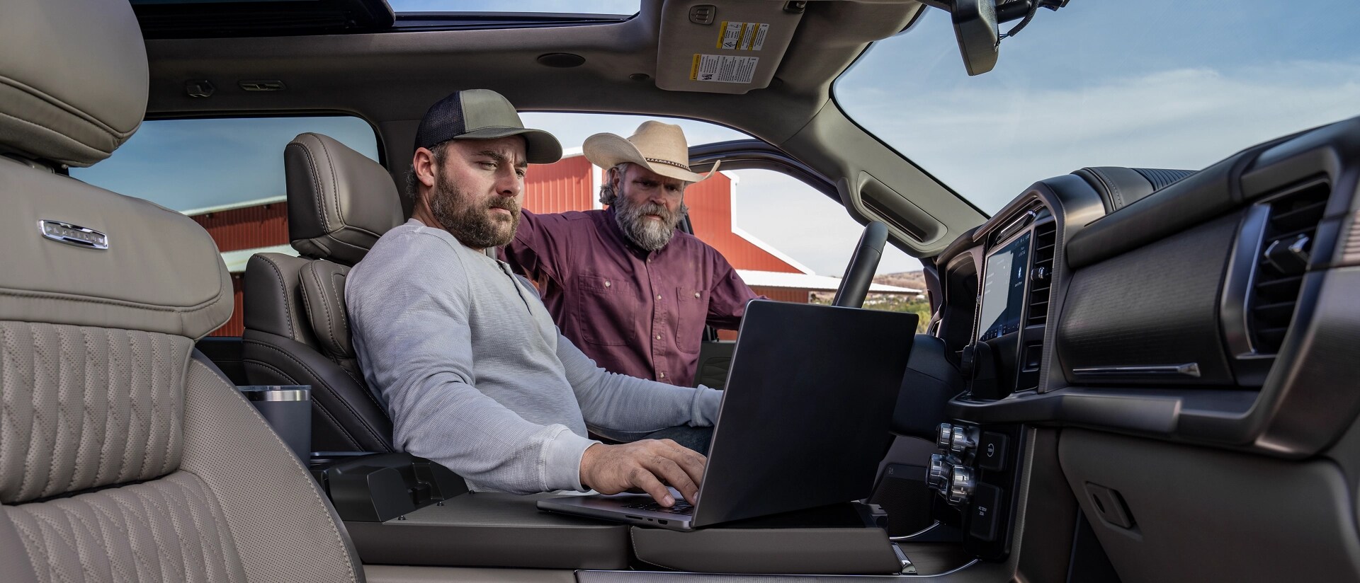 Two men looking at a laptop computer on the interior work surface of a 2026 Ford F-150® Platinum® pickup