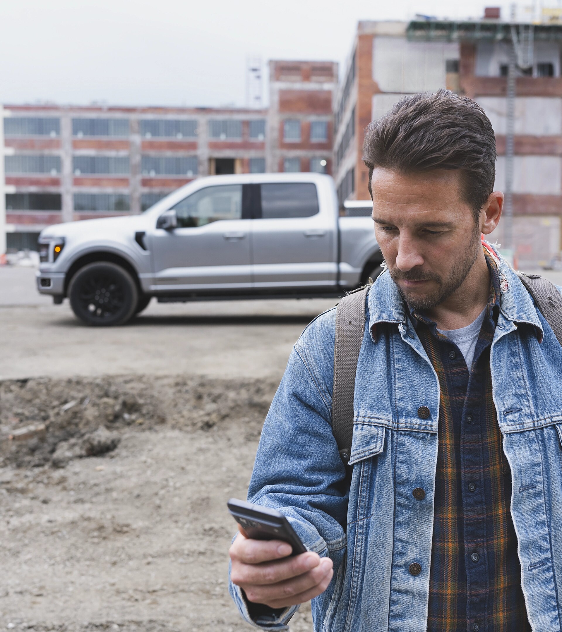 A man looking at his smartphone with an 2026 Ford F-150® pickup in the background parked at a construction site