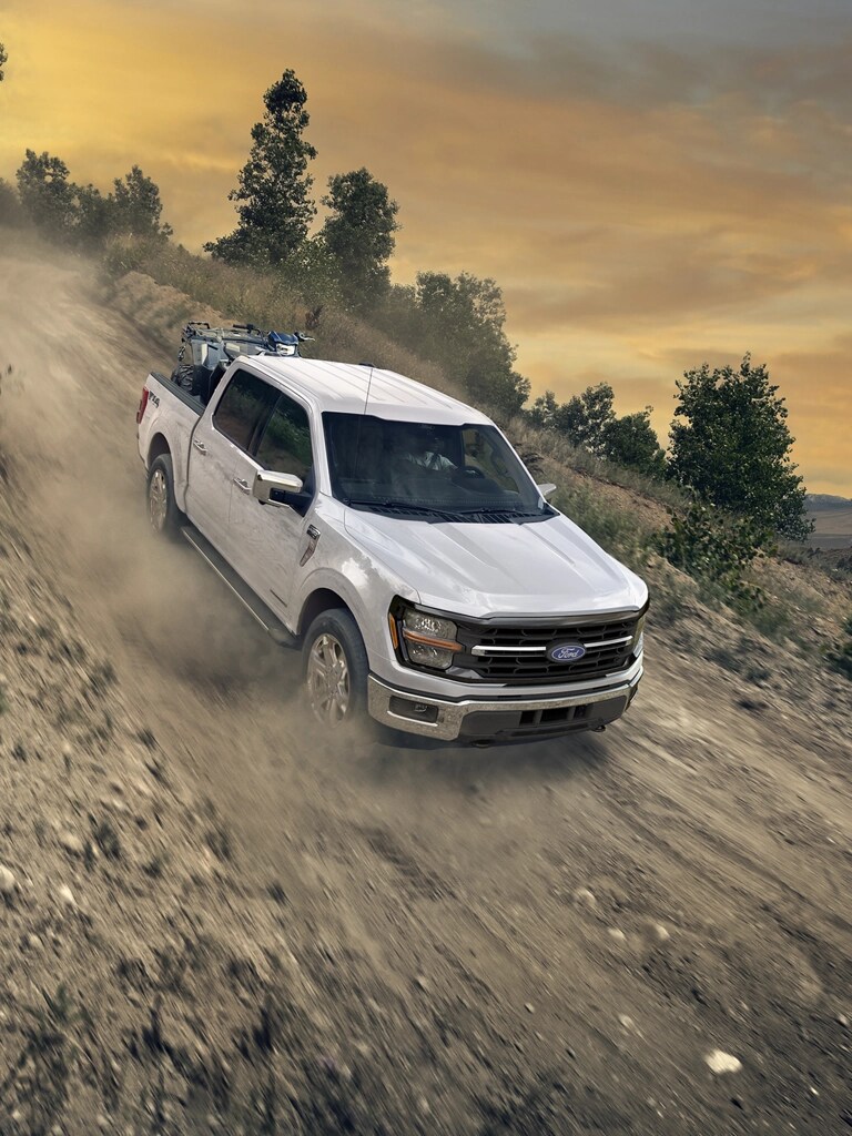 2026 Ford F-150® STX® FX4 pickup in Oxford White being driven down a dirt road with an ATV in the bed