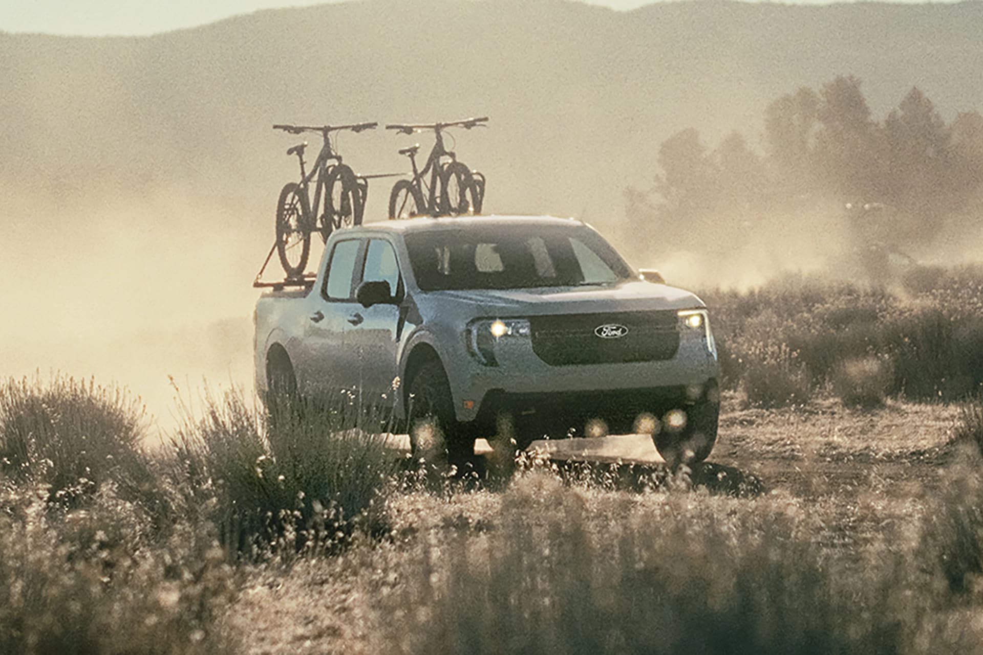 A 2025 Ford Maverick® pickup with bicycles in the truck bed is being driven on a dusty trail