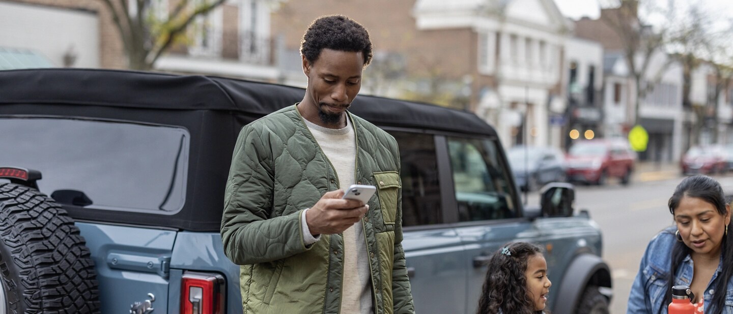 A man looks at his phone while standing beside his Ford Bronco®