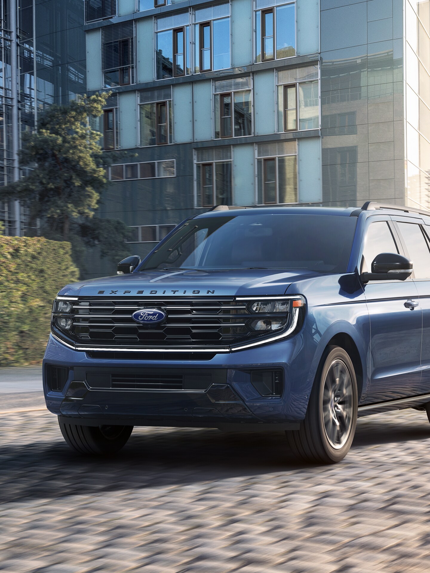 A 2025 Ford Expedition® accelerates on a brick paver road with a cityscape in the background