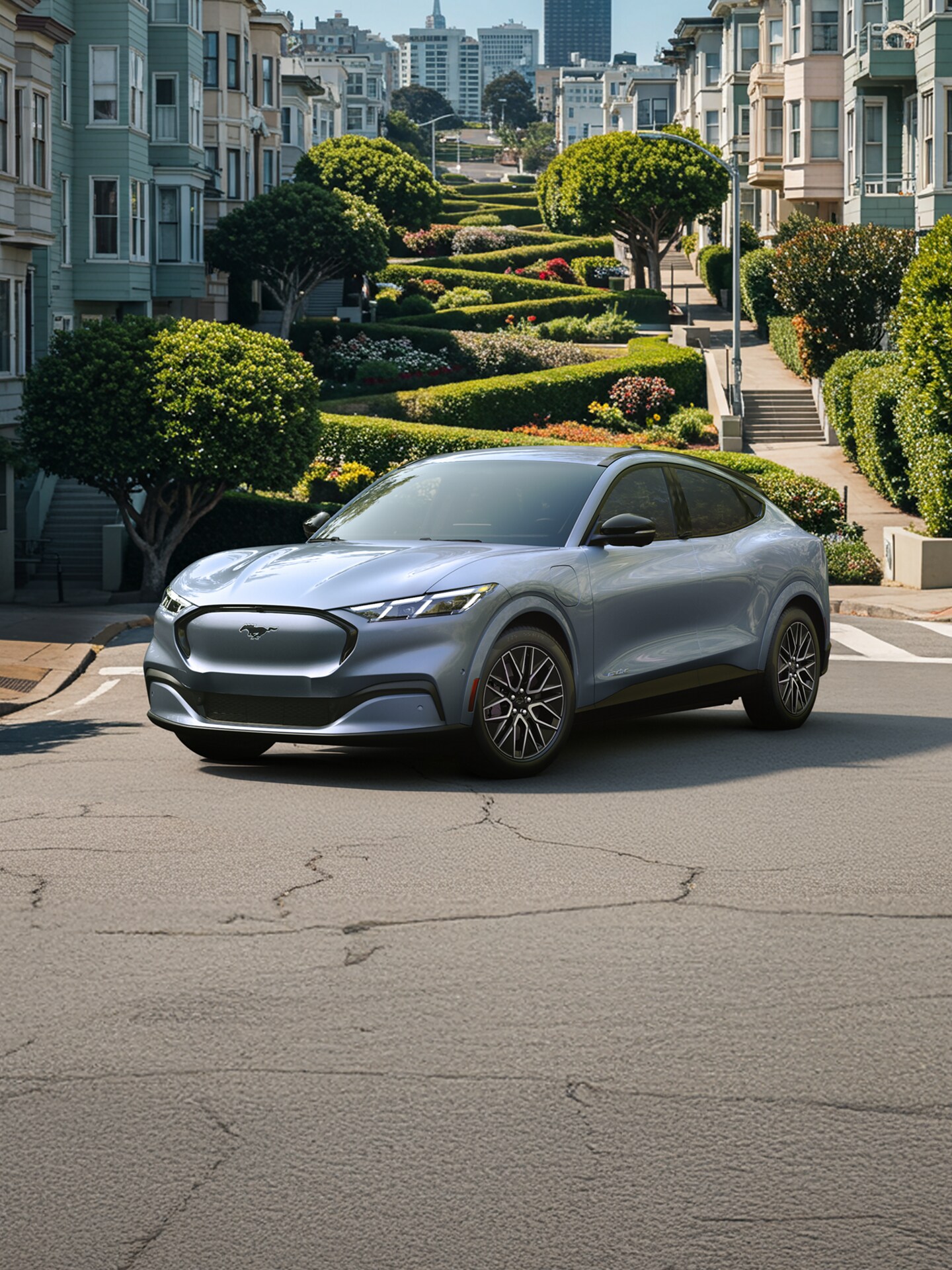 A 2025 Ford Mustang Mach-E® parked in front of a city park with flowering shrubs