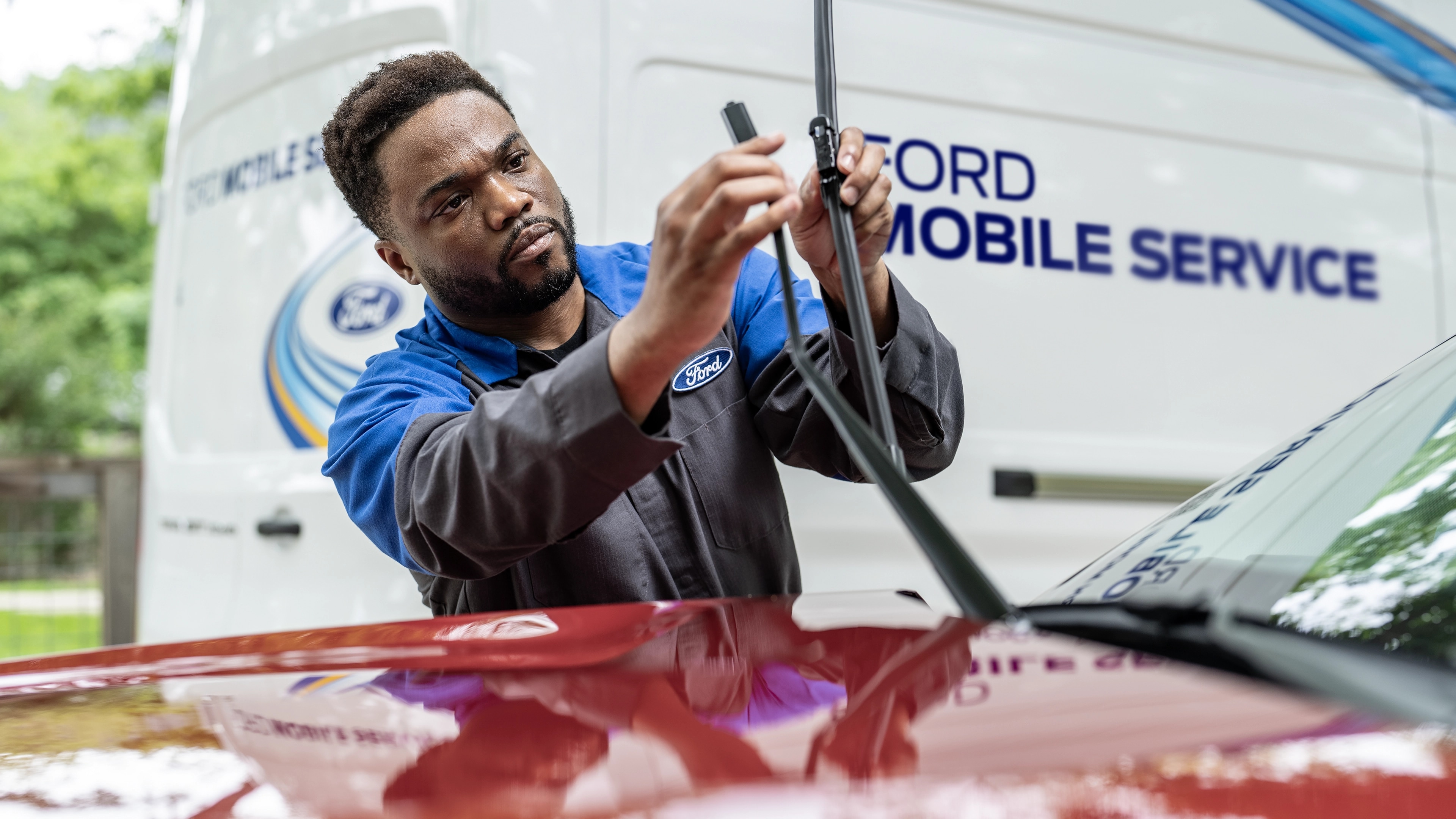 A Ford service technician changes a windshield wiper on a Ford vehicle. The Mobile Service work truck is in the background
