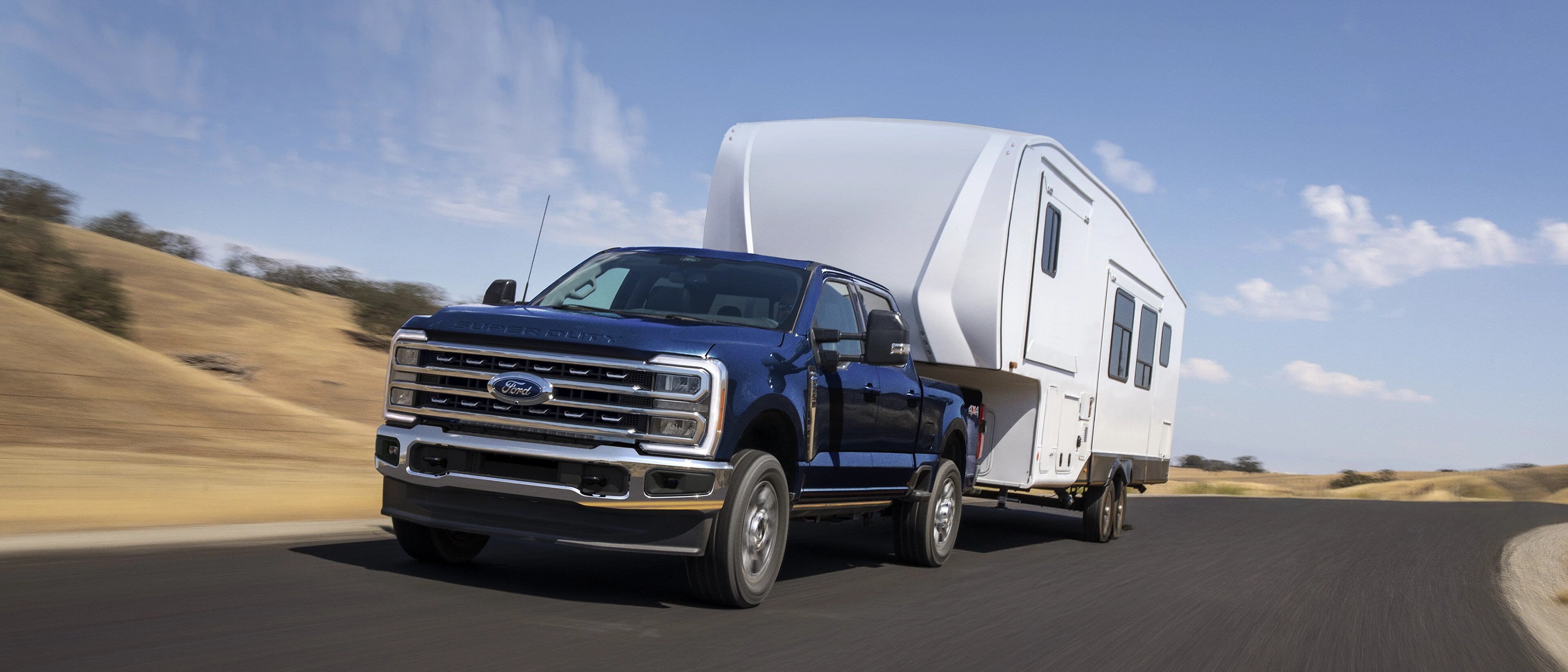 2025 Ford Super Duty® F-250® Lariat® model in Antimatter Blue pulling a large camper on a paved road